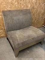 Side angled view of oversized lounge chair showing ribbed taupe upholstery and cushioned seating with wooden legs.