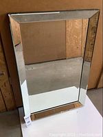 Front view of rectangular beveled mirror with black border frame leaning against wall.