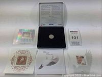 Full set including coin in black felt inset inside metal tin, four different stamps, informational text inside tin lid, and MaxSold auction tag.