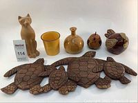 Photo showing six decorative items: three carved wooden turtles, yellow ceramic pot, wooden vase, wooden bird, and wooden cat figurine.