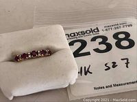 Front view of ring on white cushion showing ruby and diamond arrangement next to lot card