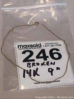 Full view of the delicate gold chain bracelet in a plastic bag with lot number and description card stating 14k 9 inch broken.