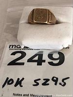 Front view of signet ring on foam pad showing rectangular top with monogram engraving and auction lot sticker