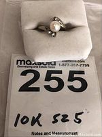 Photo of the 10k gold ring with pearl and diamonds placed on white display mount, showing front view with pearl and diamond accents.