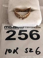 Front view of the ladies 10k gold ring resting on a white foam pad, showing the chevron V shape and filigree details. The lot number 256 tag with '10K sz 6' handwritten is visible.
