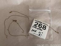 Two broken gold chains laid out with a plastic bag holding a lot number and description tag showing '10K 16"'.