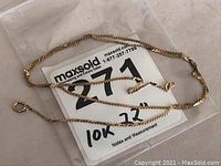 Full view of the 22 inch 10k gold ladies neck chain coiled on a flat surface with MaxSold label