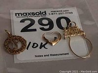 Photo showing the lot number 290 with three gold charms placed on top, includes round filigree 'P', heart-shaped charm with stone, and ring-shaped charm.