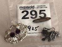 Three sterling silver items including floral brooch, dragon pin and oval engraved pin on a white background with auction label.