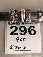 Four sterling silver ladies rings placed on a ring sizer with lot number card showing sizes 5 to 7 and 925 stamp.
