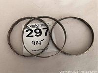 Top-down view showing three sterling silver bangles arranged on a white surface with a MaxSold lot tag marked '925'.
