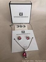 Full view of the necklace and earrings set displayed on a branded Katherine Karambelas card with a white box in the background.