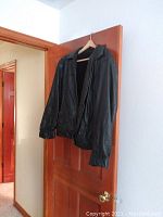Black leather coat hanging on a door, showcasing overall exterior with collar and zipper.