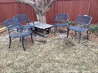 Four heavy metal outdoor chairs with black lattice and circle pattern design arranged outside, visible dirt and weathering on surfaces.