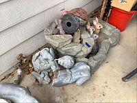 Artificial stone-like pond structure and various animal figurines placed around and inside it, showing multi-level rock design and outdoor setting.