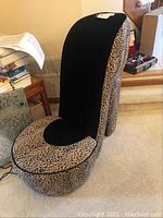 Side view of the vintage high heel shoe chair showing leopard print upholstery and black fabric heel back, placed in a carpeted room.