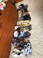 Photo showing 15 pairs of shoes arranged on the floor in various styles and sizes including men's and women's shoes, hats stacked near shoes, and some packaged shirts.