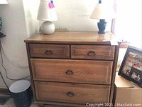 Wooden four-drawer chest beside a framed family photo and two table lamps on top