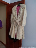 Full front view of the vintage white mink coat with belt hung on a wooden door.