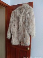 Full view of the beige/light brown Angora rabbit fur coat hanging on a door, showing front, sleeves, and length.
