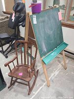 Wooden children's rocking chair and folding chalkboard easel with chalk accessories, shown in basement setting