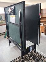 Folding ping pong table in folded position showing legs and structure in basement setting.