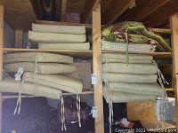 Photo showing multiple beige outdoor seat cushions stacked on wooden shelves with some cushions featuring fabric ties.