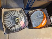 Photo of two lamps in boxes showing white ribbed lamp with brass chain on left and orange lamp with white circular grill on right.