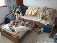 Full view of wooden trundle bed with mattresses and various blankets on top and on the pull out lower bed.