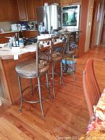 Three metal barstools aligned in front of a kitchen island on a wooden floor.