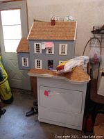 Full view of the blue dollhouse on top of a white appliance near a door.