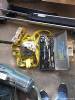 Delta rain showerhead, yellow ratchet strap, socket set in metal case, furniture feet, and other items on floor.