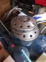 Four stacked metal 20 inch wheel covers with hole patterns, placed on water jugs with a kids bike in background