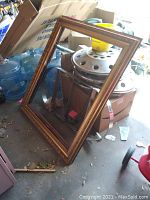 Full view of the largest wood picture frame showing its size and style leaning against metal and boxes.