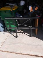 Side view of rectangular metal automotive cargo rack with clamp mounts and tubular canopy frame supports, black/dark gray color.