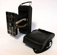 Kodak Jiffy camera extended next to its black carrying case, showing the camera bellows, metal support arms and the design on the camera front.