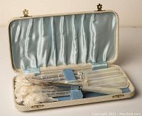 Open case displaying six knives with faux-pearl handles and stainless steel blades wrapped in paper inside a blue satin-lined case.
