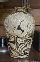 Front and side view of large brown and beige pottery vase with floral relief design on wooden background.