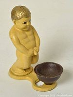 Front view of a yellow metal boy statue bottle opener with a brown bowl-shaped section attached to the base.