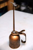 Front view of vintage metal oiler with long curved spout, showing patina and pump trigger