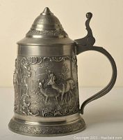 Side view of pewter beer stein showing deer hunting scene with ornate borders and textured background