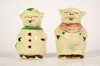 Front view of two ceramic pig salt and pepper shakers showing distinct scarves and facial expressions