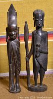Front view of two carved wooden statues from Tanganyika placed against a colorful textile background.