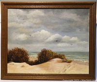 Front view of the signed oil painting showing the seascape scene with dunes, sea grasses, ocean, and cloudy sky in a wood frame.