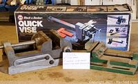 Photo showing three vises including boxed Black & Decker Quick Vise and two bench vises on table with measuring tape for scale.