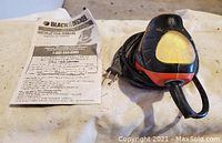 Black and Decker mouse sander shown from a side angle with the instruction manual beside it.