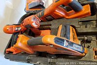 Photo showing two cordless power tools, one identifiable as a drill and the other a handheld tool, inside a hard black molded carry case.