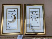Pair of framed handmade paper art pieces showing moon and sun motifs, gold frames with white mats, approximate size 10x16 inches each