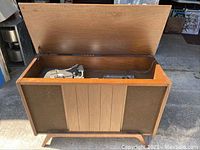 Open vintage wooden stereo cabinet with front panel and legs visible in sunlight.