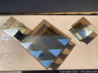 Three mid century modern style wall mounted candleholders with mirrored glass surfaces. One large central piece and two smaller side pieces. Items show dirt and dust and require cleaning. Mounted with hangers on the back for wall display.
